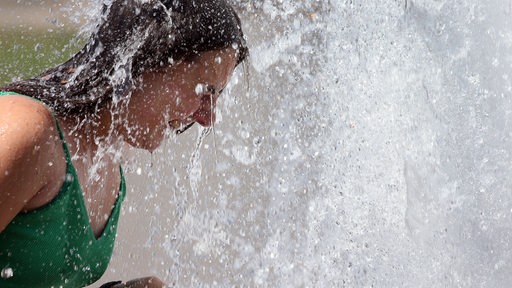 Eine junge Frau sucht bei sommerlicher Hitze Abkühlung in einem Citybrunnen
