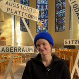 Eine Frau sitzt auf einem Stuhl in einer Kirche vor vier Wegweisern