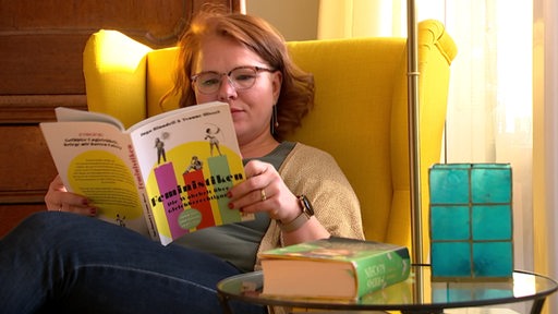 Die Soziologin Ruth Müntinga sitzt in einem gelben Sessel und ließt in einem feministischen Buch.