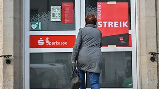 Eine Frau steht vor der Tür der Sparkasse, an der ein Transparent mit der Aufschrift "Heute: Streik" hängt.