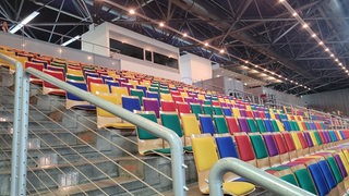 Blick auf eine Tribüne mit bunten Plastiksitzen in einer Halle.