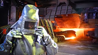 Ein Mitarbeiter in Schutzkleidung steht beim Abstich von Roheisen an einem Hochofen 