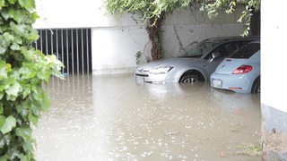 2 Autos stehen an einem Gebäude unter Wasser.