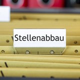 Auf einem Schild an einer Aktensammlung steht das Wort "Stellenabbau".