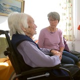 Eine Sterbebegleiterin sitzt neben einer alten Frau.