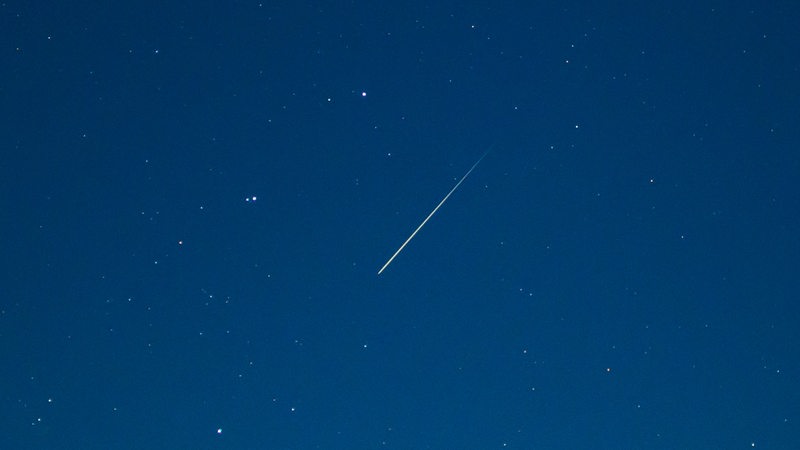 Eine Sternschnuppe leuchtet am Sternenhimmel.