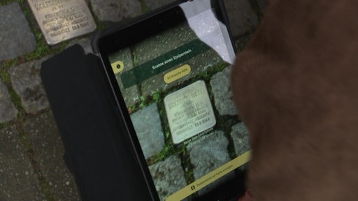 Mit einem Tablet wird ein Stolperstein gescannt.