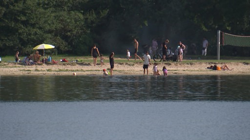 Blick vom See auf den Strand, wo einige sich sonnen oder schwimmen gehen.