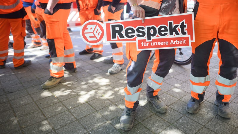 Bauarbeiter halten ein Schild "Respekt für unsere Arbeit" in den Händen