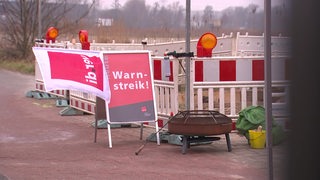 Neben Baustellenabsperrungen steht ein Schild mit der Aufschrift "Warnstreik", an dem eine Flagge von Verdi weht.