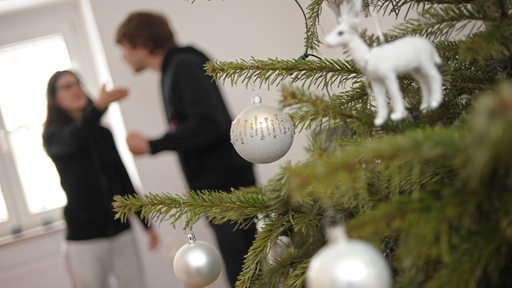 Ein Pärchen streitet sich hinter einem Weihnachtsbaum