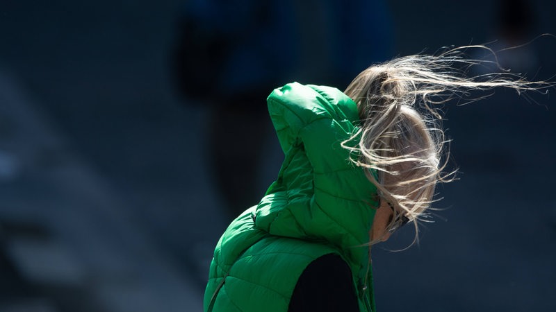 Eine Frau im im Wind, der Wind drückt ihre Kapuze gegen ihren Kopf, ihre Haare wehen.