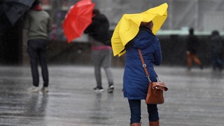 Passanten schützen sich mit Regenschirmen vor starkem Wind (Archivbild)