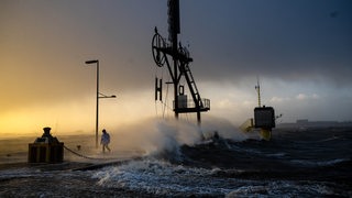 Ein Spaziergänger läuft bei Sturmflut und Wellen am Ufer der Wesermündung in Bremerhaven entlang.