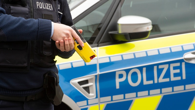 Ein Polizist hält einen gelben Taser in der Hand.