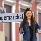 Patricia Friedek steht vor einem Schild mit der Aufschrift "Langemarckstraße"
