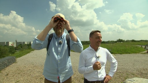 Der Journalist Nils Braunöhler blickt durch ein Fernglas, neben ihm steht der Tourismuschef der Stadt Bremerhaven Michael Gerber.