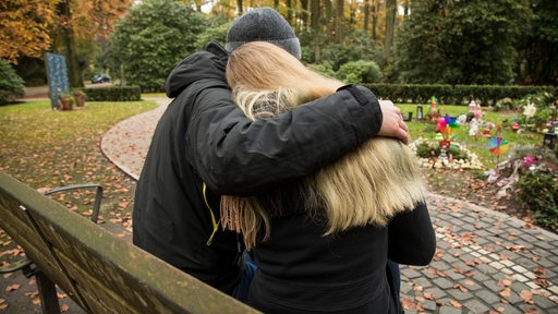 Ein Paar sitzt trauernd auf einer Bank auf dem Friedhof.