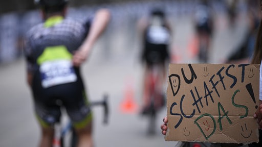 Zuschauer hält Schild mit Aufschrift "Du schaffst das", Rennradfahrer im Hintergrund