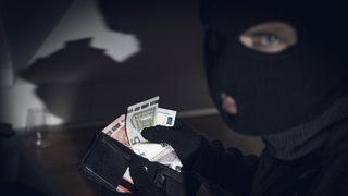 Ein maskierter Mann nimmt Geld aus einem Portemonnaie