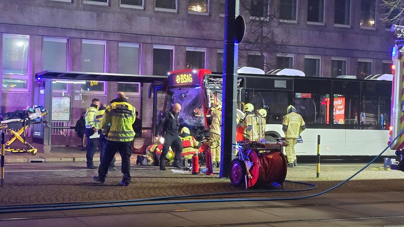 Einsatzkräfte stehen um einen Bus, der an der Front beschädigt ist.