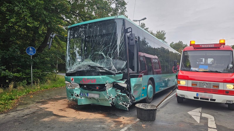 Ein Linienbus mit beschädigter Front steht auf einer Straße neben einem Rettungsfahrzeug.