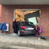 Ein Auto steht zwischen Kleiderständern und Scherben in einem Schaufenster.