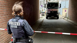 In einer Einfahrt steht ein Müllwagen, davor ist eine Polizistin zu sehen.