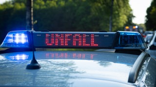Ein Einsatzfahrzeug der Polizei steht mit Blaulicht und dem Schriftzug Unfall im Display an einem Unfallort.