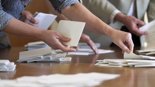 Menschen zählen Stimmzettel während einer Wahl auf einem Tisch aus