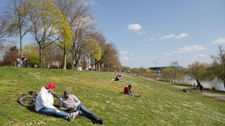 Menschen genießen die Sonne am Osterdeich an der Weser, hinten das Weserstadion