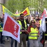 Mehrere Menschen nehmen in gelben Warnwesten und mit Fahnen an einem Streik teil.