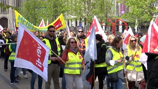 Mehrere Menschen nehmen in gelben Warnwesten und mit Fahnen an einem Streik teil.