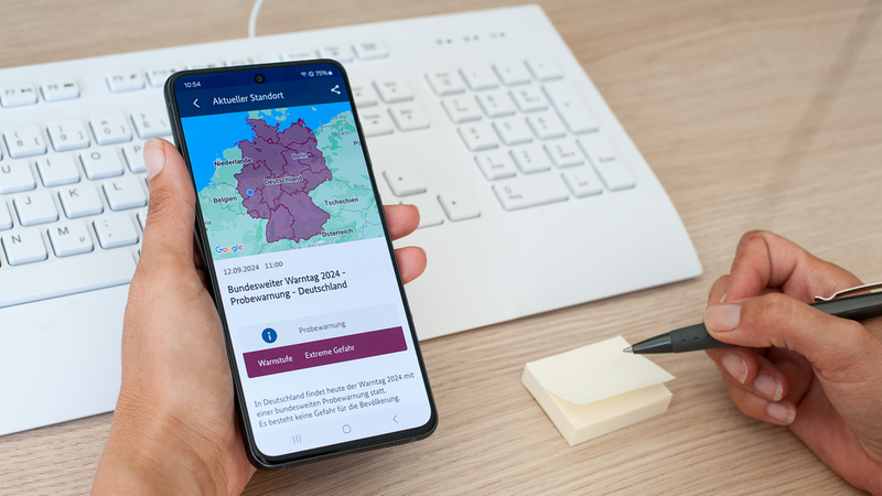 Handy vor Tastatur mit Deutschlandkarte und Warnmeldung.