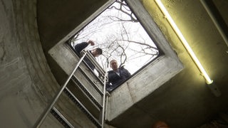 Zwei Handwerker schauen von oben in den Einstieg zu den Pumpanlagen.