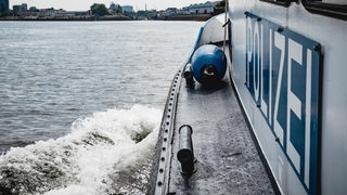 Ein Boot mit der Aufschrift Polizei fährt übers Wasser, am Ufer stehen Gebäude.