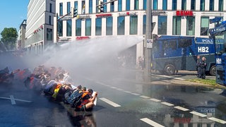 Menschen sitzen auf der Straße und werden von zwei Wasserwerfern getroffen.