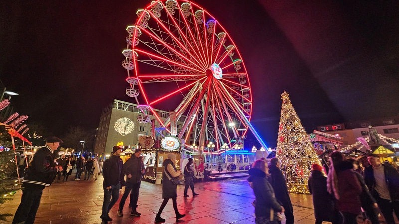 Mehrere Menschen laufen über einen Platz vor einem Riesenrad.