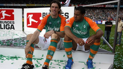 Die damaligen Werder-Spieler Mladen Krstajic und Ailton sitzen nach der Übergabe der Meisterschale auf einem Podium.