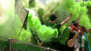 Mehrere Werder Bremen Fans in einem Stadion umhüllt von grünem Rauch verursacht durch Pyrotechnik