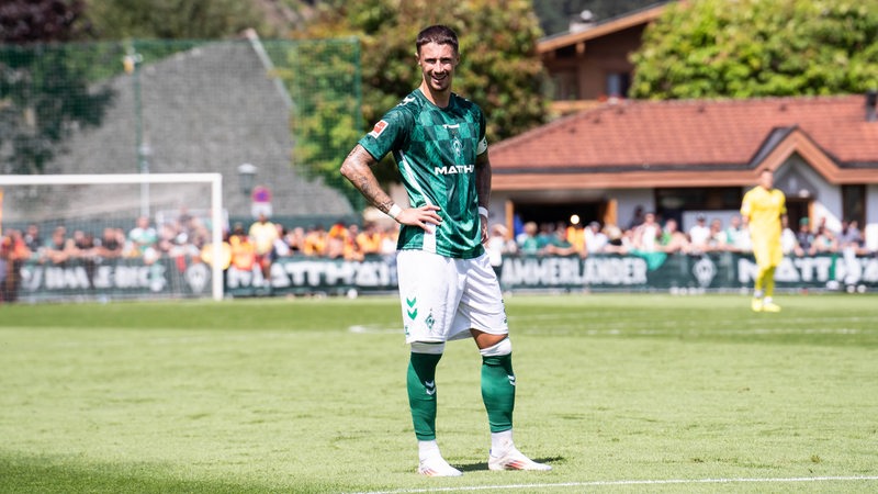 Werder-Kapitän Marco Friedl steht auf dem Platz und stemmt die Hände in die Seiten.