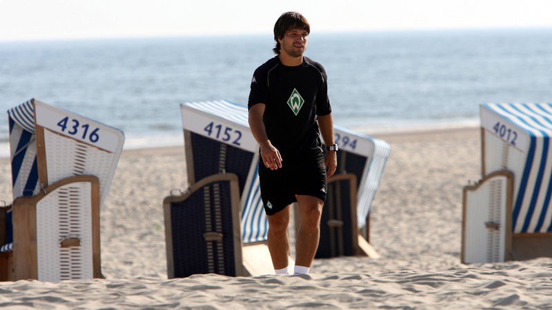 Diego läuft auf Norderney am Strand entlang. Hinter ihm sind Sand, Strandkörbe und das Meer zu sehen.