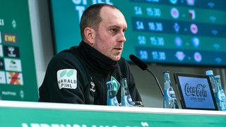 Ole Werner sitzt bei der Pressekonferenz und spricht ins Mikrofon.