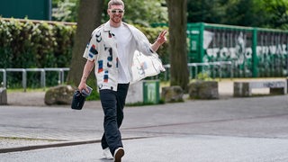 Mitchell Weiser läuft in Freizeitkleidung und mit Sonnenbrille am Weser-Stadion entlang.