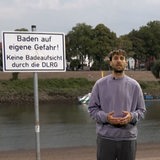 Ein junger Mann, Max Lange, steht vor einem Schild "Baden auf eigene Gefahr"