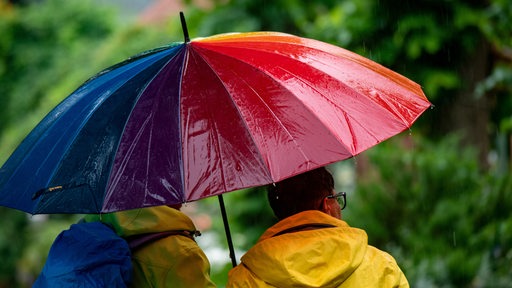Spaziergänger sind bei Regenwetter mit einem bunten Regenschirm unterwegs.