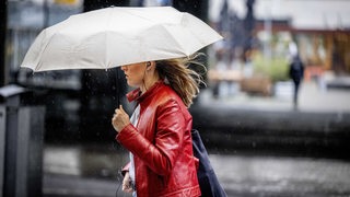 Eine Frau mit Regenschirm geht die Straße entlang, Haare fliegen im Wind.