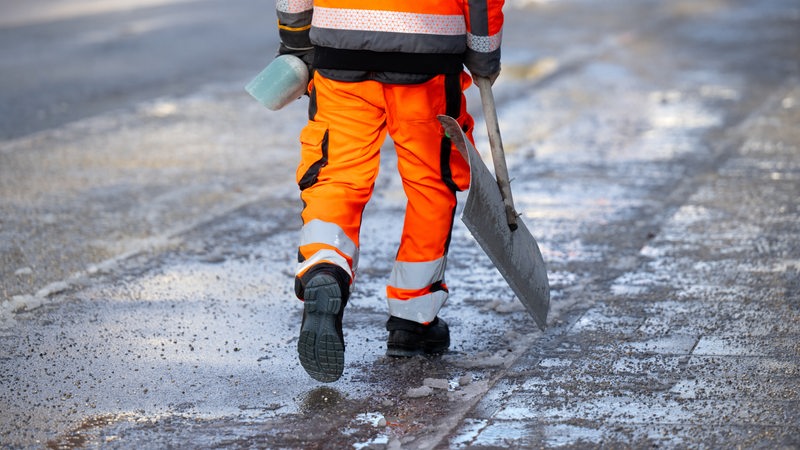 Ein Mitarbeiter vom Winterdienst geht mit einer Schneeschaufel über einen geräumten und gestreuten Fußweg.