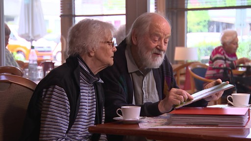 Zwei ältere Personen sitzen an einem Tisch und betrachten ein Foto.