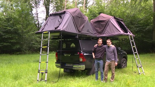 Die Jugunternehmer Immanuel Schneider und Jakob Heider stehen vor einem Auto mit einem Dachzelt drauf. 